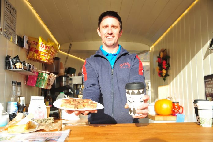Coffee 51 - 075 Man at a coffee kiosk holding a paper cup of tea and tray bake