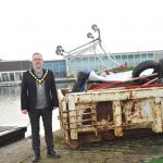 Man standing beside a skip filled with rubbish near a lake