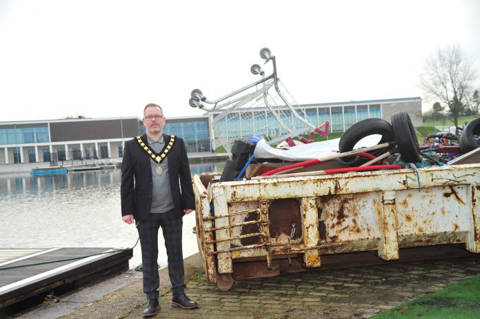 Man standing beside a skip filled with rubbish near a lake