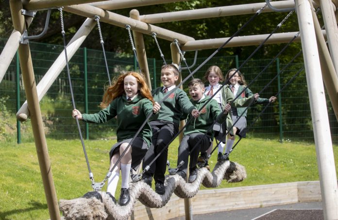 three school girls and two school boys play on new play park equipment
