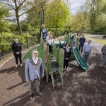 Four males, three females and four kids standing beside new equipment at play park