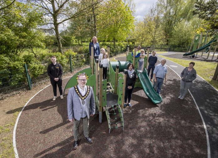 Four males, three females and four kids standing beside new equipment at play park