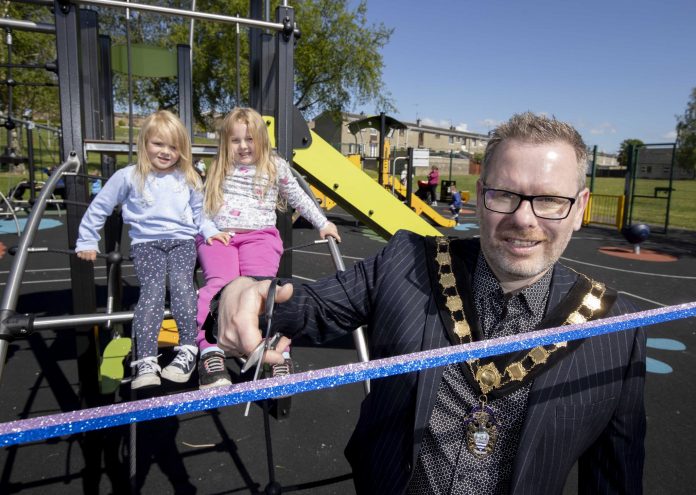 Male Lord Mayor cuts ribbon to new play park with two young girls in background