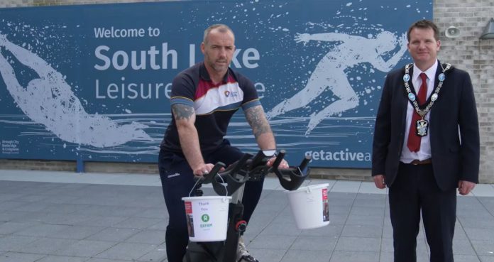 One man on a spin bike and one man standing outside