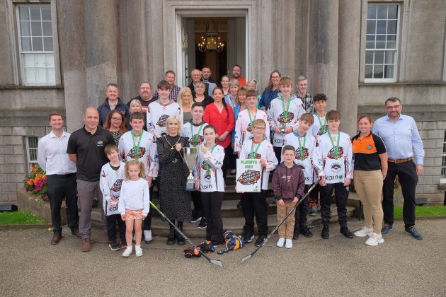 Large group of people with some holding a trophy and hockey sticks.