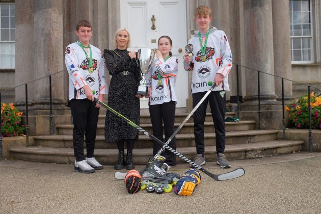 Four people standing outside holding a trophy and hockey sticks.