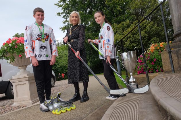 Three people standing outside with trophy and hockey sticks.