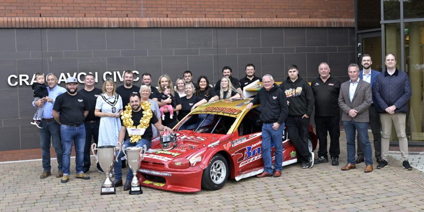 Large group of people pictured beside a racing car.