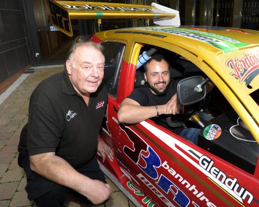 Two males, one pictured inside a racing car and one pictured outside it.