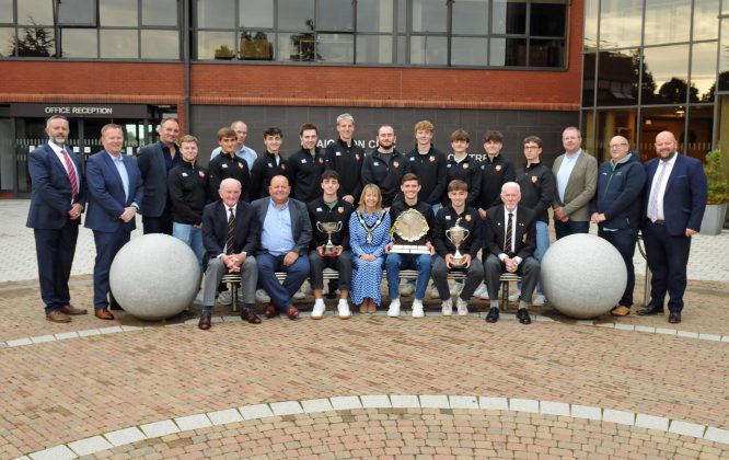 Large group of men and women outside with three trophys.