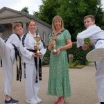 Two males doing a Taekwondo kick and two females holding a trophy.