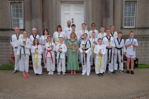 Large group of males and females holding trophies outside a council building.