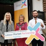 Three people standing holding a sign for Labour Market Partnerships