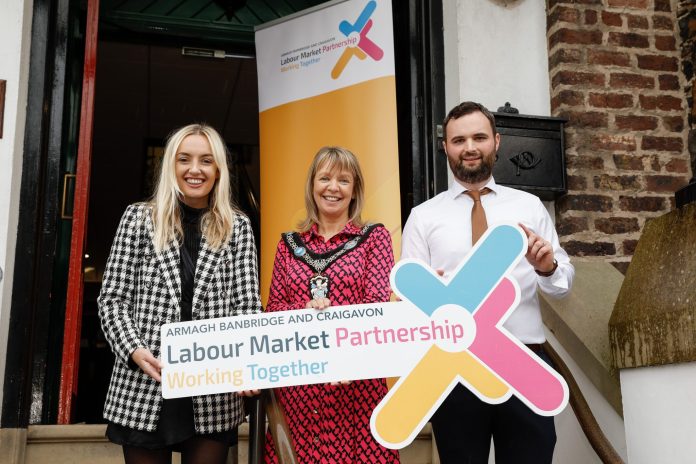 Three people standing holding a sign for Labour Market Partnerships