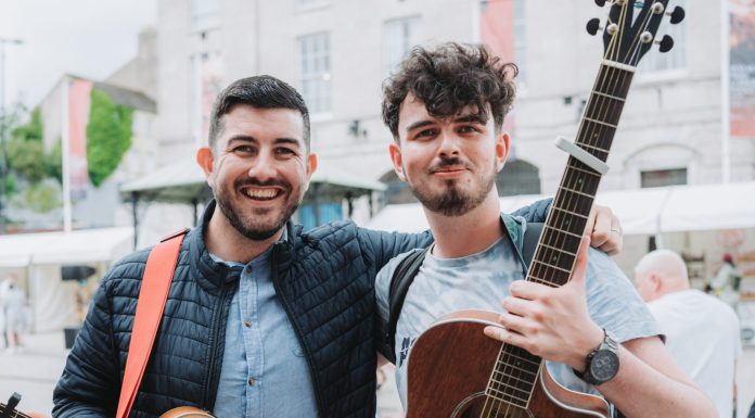 Two young men holding guitars on the street for Food and Cider Festival.