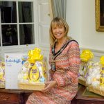 Female sitting beside easter baskets that are filled with chocolate and a toy.