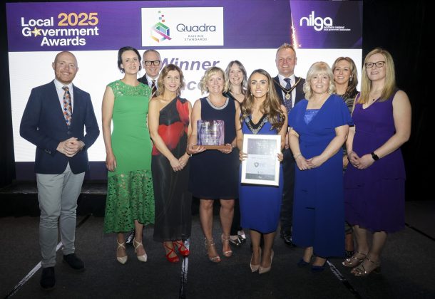Large group of people standing on the stage at an awards ceremony and two people at the front are holding awards.