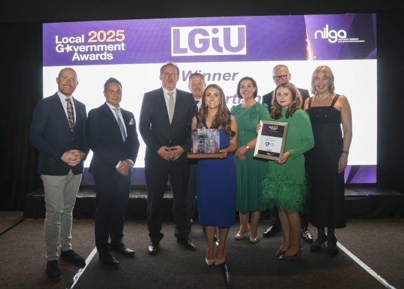 Large group of people on stage at the local government awards with two females holding awards.