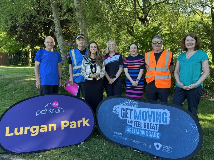 20250517_082922474_iOS Group of people standing behind signs to promote the new Lurgan Park Parkrun and Get Moving ABC.