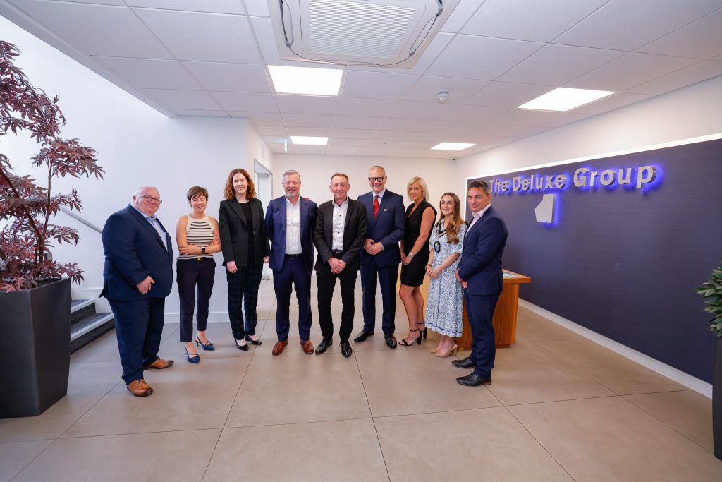 A group of people standing in a reception area with The Deluxe Group sign.