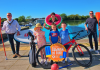 Group or people smiling in the sunshine with a range of watersports equipment and sports equipment.