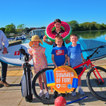 Group or people smiling in the sunshine with a range of watersports equipment and sports equipment.