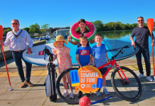 Group or people smiling in the sunshine with a range of watersports equipment and sports equipment.