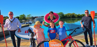 Group or people smiling in the sunshine with a range of watersports equipment and sports equipment.