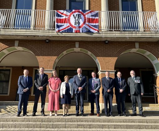 Men and women standing outside beside a flag.