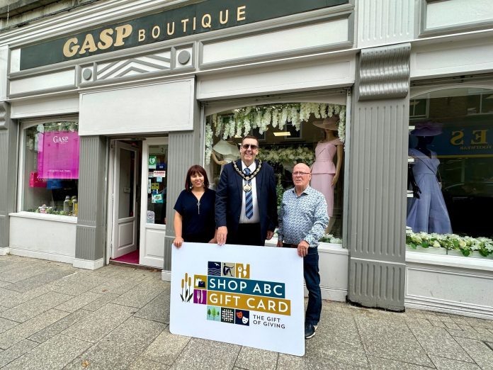Three people standing outside Gasp Boutique clothes shop with a sign saying Shop ABC Gift Card