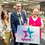 Three people standing in a cafe holding a sign saying Spark It