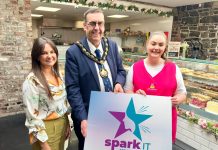 Three people standing in a cafe holding a sign saying Spark It