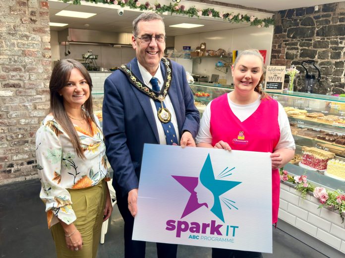 Three people standing in a cafe holding a sign saying Spark It