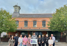 A group of people standing in Dromore Market Square with the hall and clock in the background. In the middle of the group, the Lord Mayor is holding a sign saying High Street Heroes NI 2025.