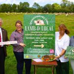 Four people standing in a field with food and a sign saying Lamb and Local.