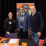 Three people standing in front of a sign at a careers fair