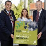 Three people holding a board that has details of the employability and skills conference taking place in Craigavon.
