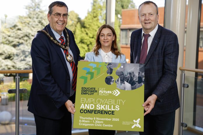 Three people holding a board that has details of the employability and skills conference taking place in Craigavon.