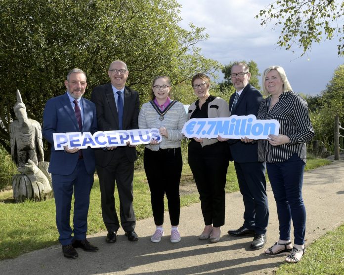 Six people stand in a row holding two signs reading PEACEPLUS and 7.7 Euro million.