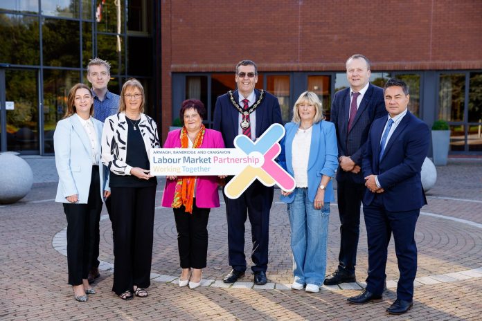 A group of people standing outside a building holding a sign that says Armagh City, Banbridge and Craigavon Labour Market Partnership.