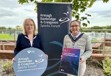 Two women standing in front of an ABC Sports Forum pop up banner and holding signs to promote the Coach Education and Club Development programme.