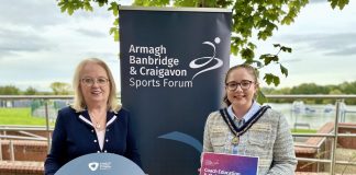 Two women standing in front of an ABC Sports Forum pop up banner and holding signs to promote the Coach Education and Club Development programme.