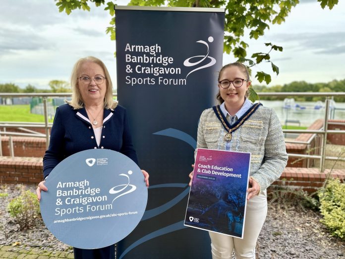 Two women standing in front of an ABC Sports Forum pop up banner and holding signs to promote the Coach Education and Club Development programme.