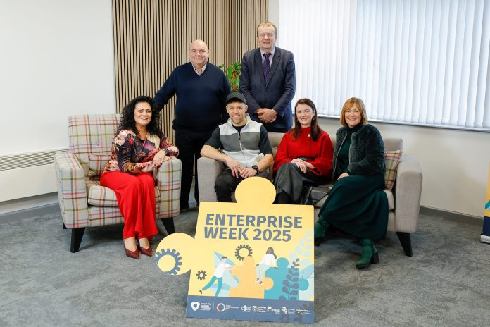 0139_ABC_Enterprise_211125 A group of people, some sitting on a sofa and some standing behind. There is a sign in front of them which reads, Enterprise Week 2025.