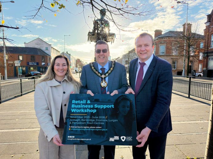 5327.-RETAIL-BUSINESS-WORKSHOP-PHOTO-PROP-EDIT Three people standing on Lurgan Plaza holding a sign that says Retail & Business Support Workshops
