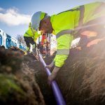 A man in high visibility workwear and hard hat, laying cables in the ground