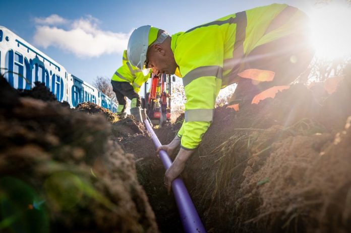 Fibrus image A man in high visibility workwear and hard hat, laying cables in the ground