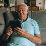 Older male sitting on a sofa using a tablet.