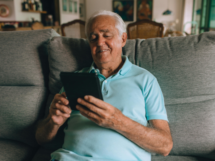 Older male sitting on a sofa using a tablet.