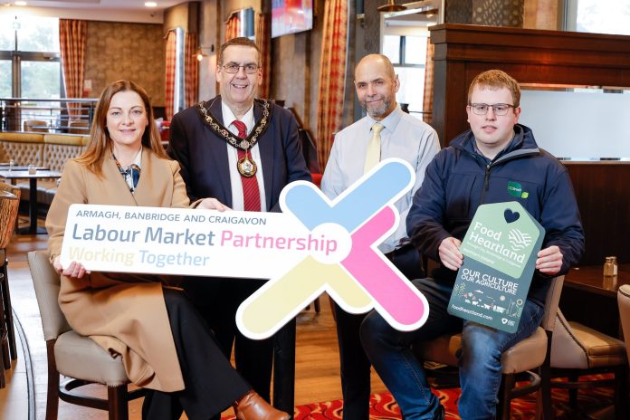 Launch of the Agri food careers fair taking place in Armagh City Hotel Four people standing in a bar restaurant holding a sign that says Labour Market Partnership